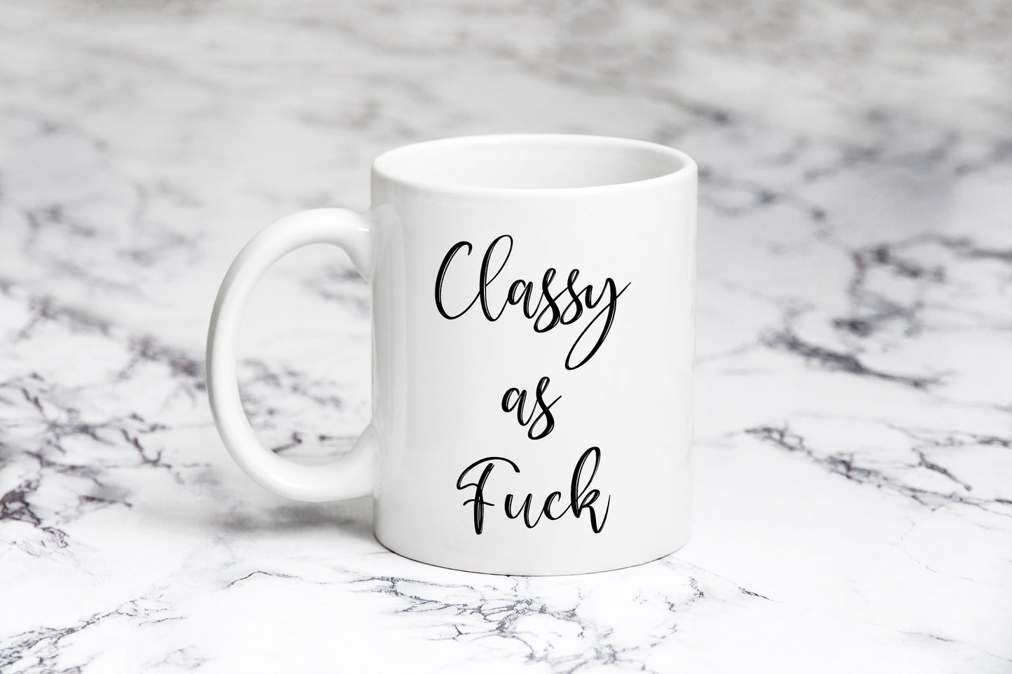 A white ceramic mug with the text 'CLASSY AS FUCK' printed in black on a marble surface.