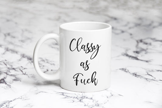 A white ceramic mug with the text 'CLASSY AS FUCK' printed in black on a marble surface.